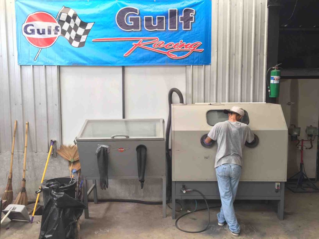 Young man sand blasting a Harley Davidson 45 cylinder head.